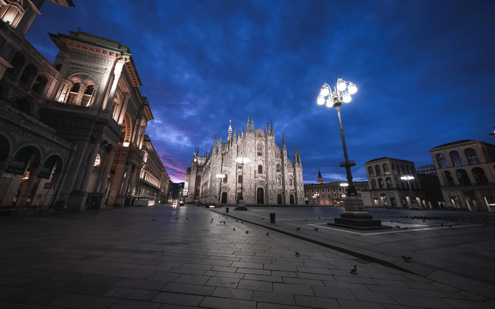 Milan's Duomo cathedral and piazza lit at blue hour, empty streetlamp in the foreground (representative photograph of Milan by night — Maison Milano itself is south of the centre, in Chiesa Rossa)