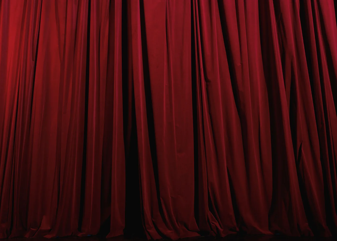 A rich red pleated theatre curtain, lit close and dramatic (representative photograph of a theatre-restaurant stage curtain, not Maison Milano's own room)
