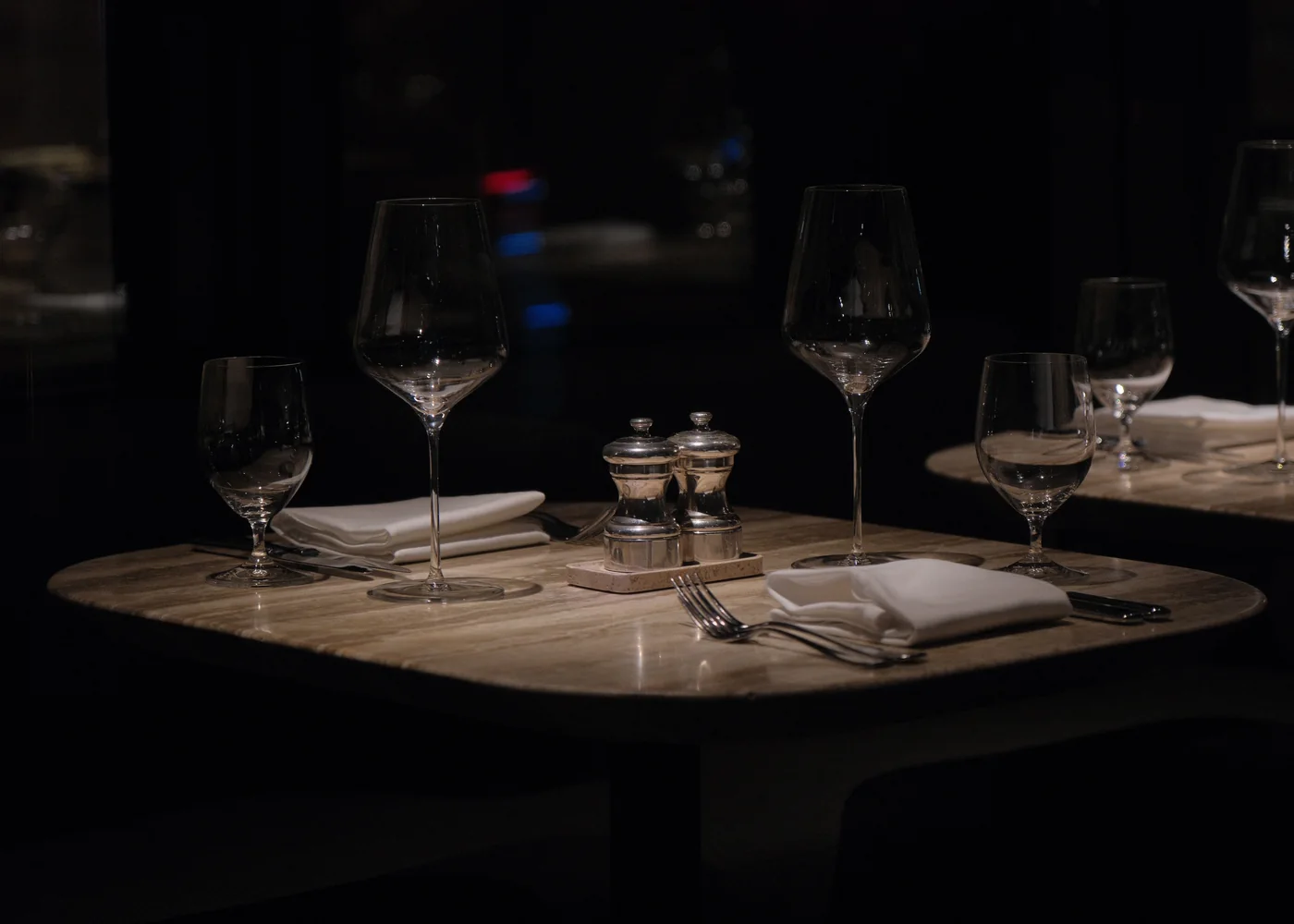 A dark, elegant restaurant table set with wine glasses and folded napkins (representative photograph of a dinner-theatre table setting, not Maison Milano's own room)